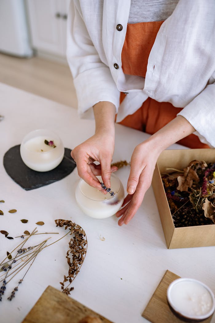 our-services-3 Hands crafting candles with dried flowers in an artisanal workshop setting.